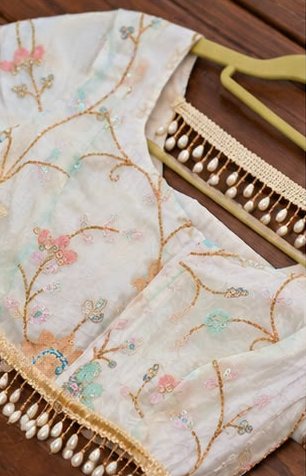 Ivory blouse with pastel floral embroidery and pearl drop edging, on a hanger